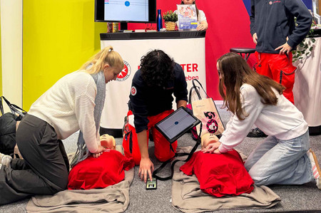 Zwei Messebesucherinnen machen das Reanimationsduell, angeleitet von einem Johanniter-Zivildiener.