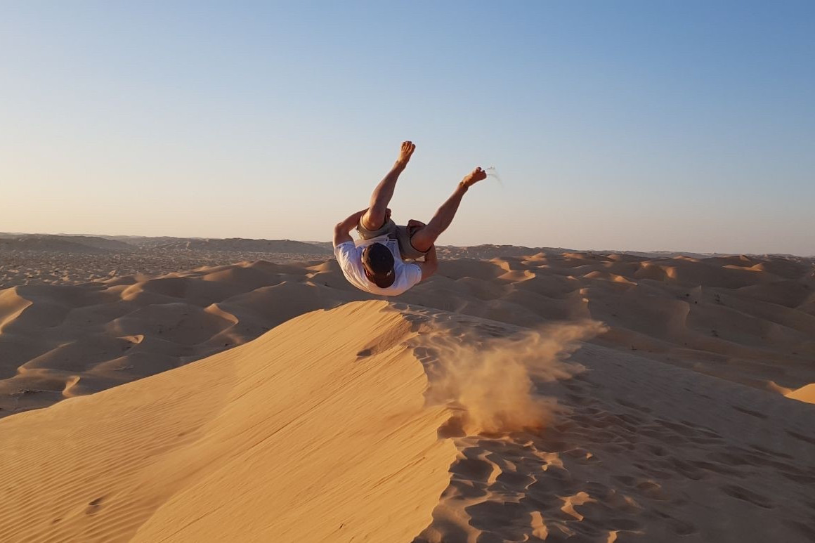 Ein Mann, Denis, macht einen Salto auf einer Düne in der Wüste.