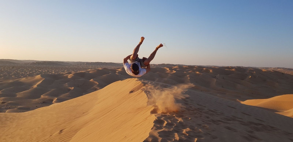 Ein Mann, Denis, macht einen Salto auf einer Düne in der Wüste.