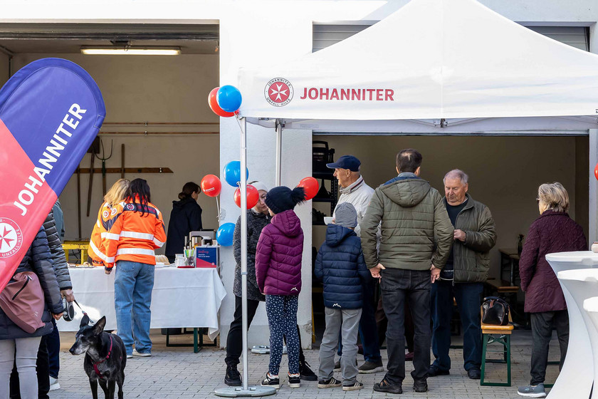 Gäste beim Tag der offenen Tür stehen im dekorierten Hof der Johanniter unter einem Zelt.