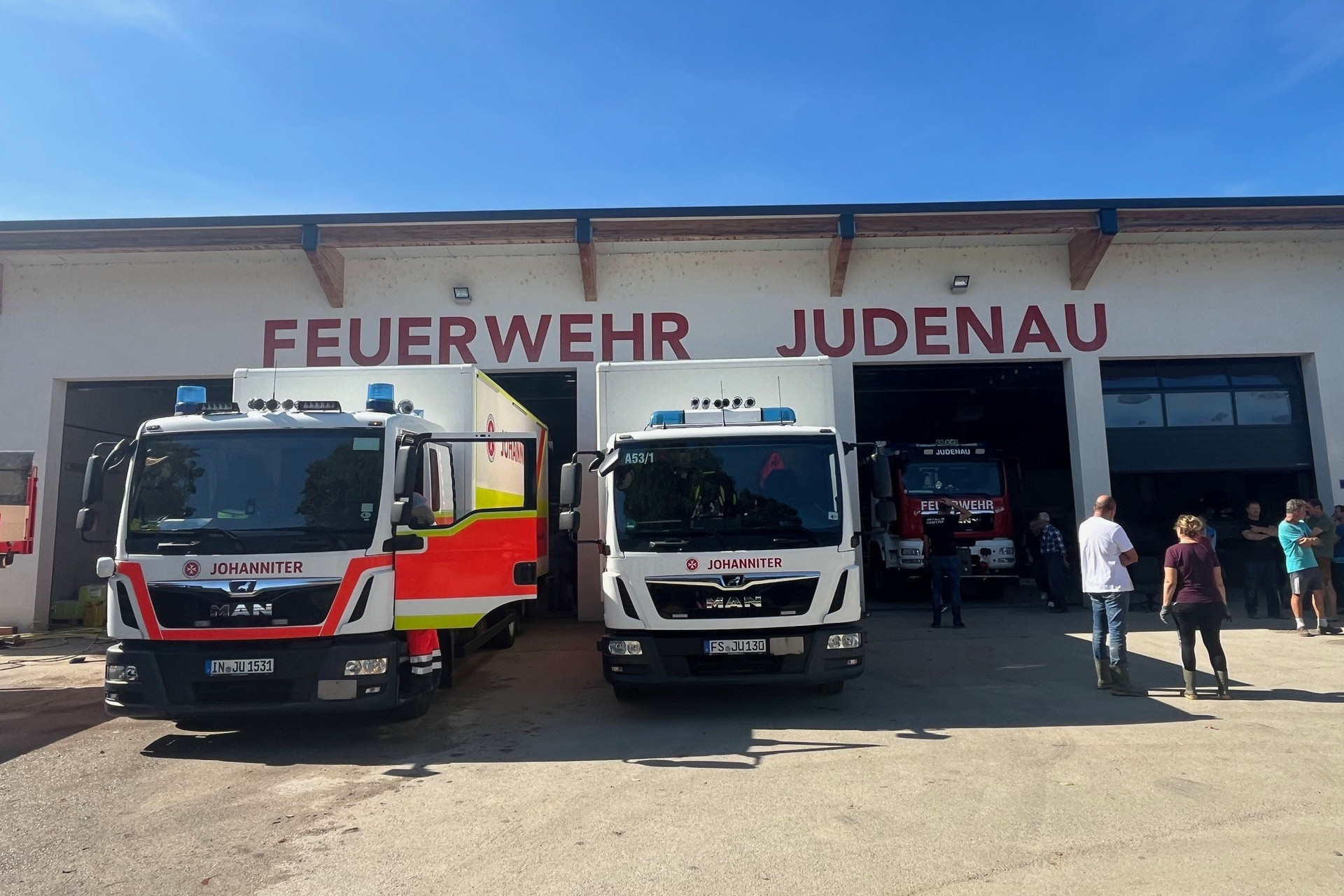 Zwei LKWs der Johanniter stehen vor einem Feuerwehr-Gebäude, um Trocknungsgeräte anzuliefern.
