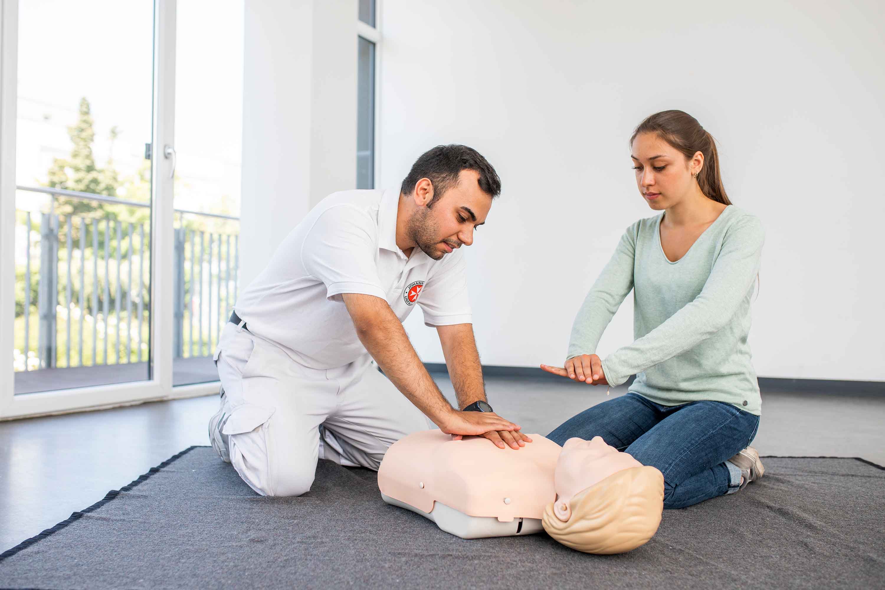 Eine Frau übt unter Anleitung des Kursleiters die Wiederbelebung an einer Puppe.
