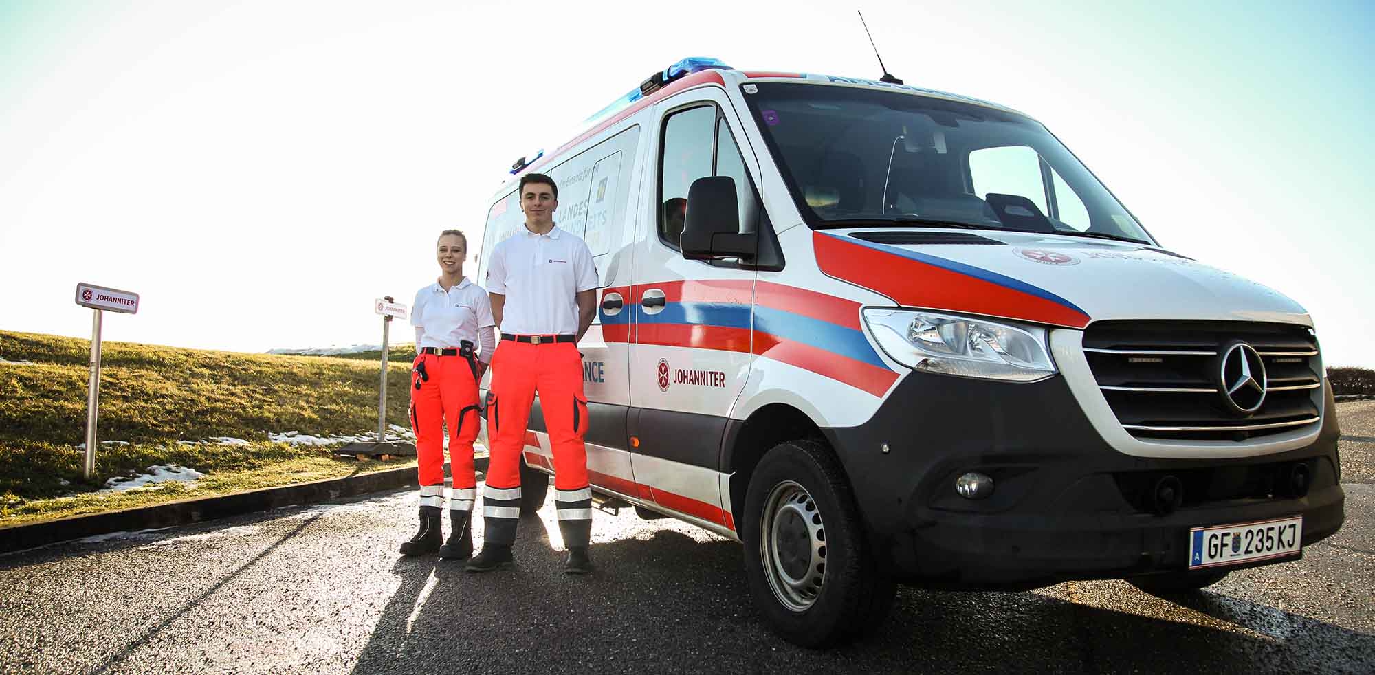 Ein Team von zwei Johannitern steht neben einem Einsatzauto der Johanniter.