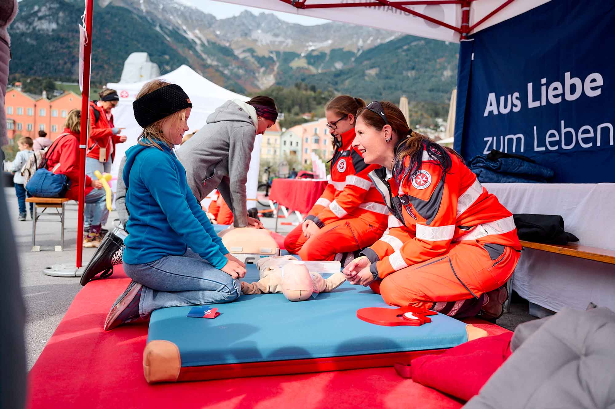 Eine Johanniterin erklärt einem Mädchen die Reanimation an einem Säugling.