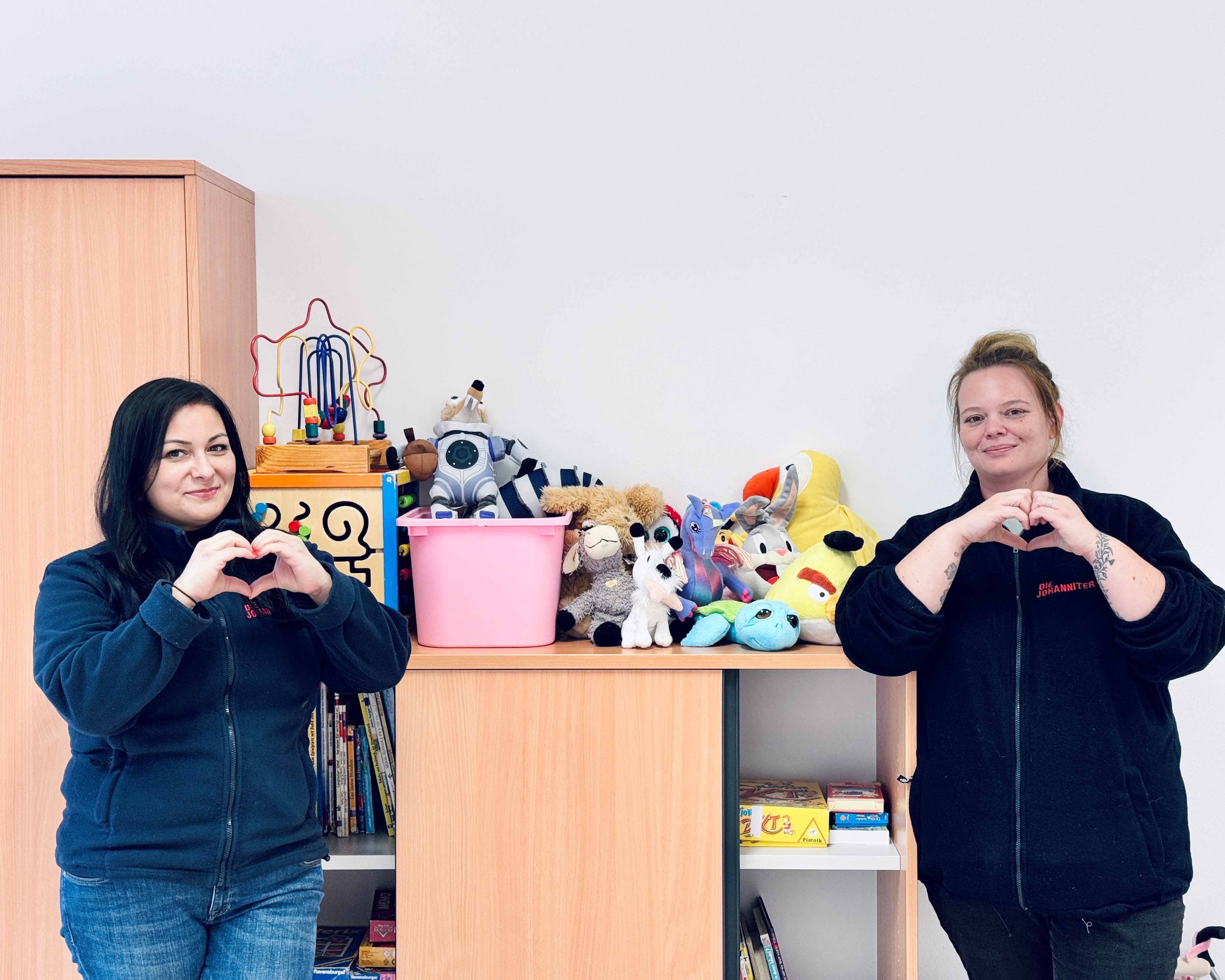 Zwei Betreuerinnen zeigen ein Herz in die Kamera, als Danke-Zeichen für die Spielzeugspenden