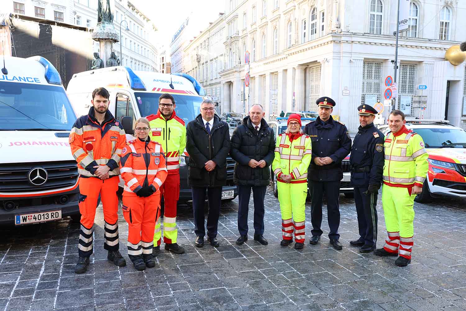 Die "Vier für Wien" stehen gemeinsam mit Polizei und Vertretern der Politik vor Rettungsautos.