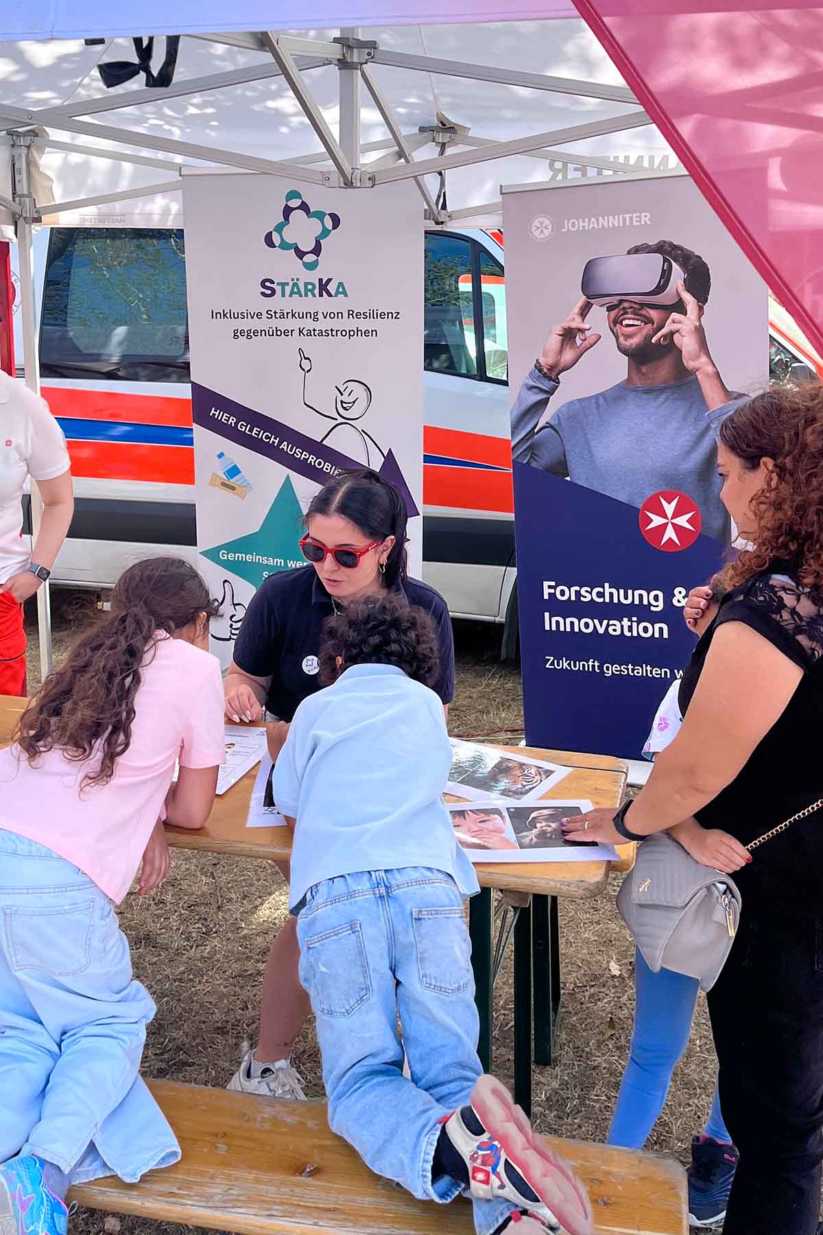 Eine Johanniterin erklärt zwei Kindern spielerisch ein Forschungsprojekt zum Thema Katastrophenschutz.