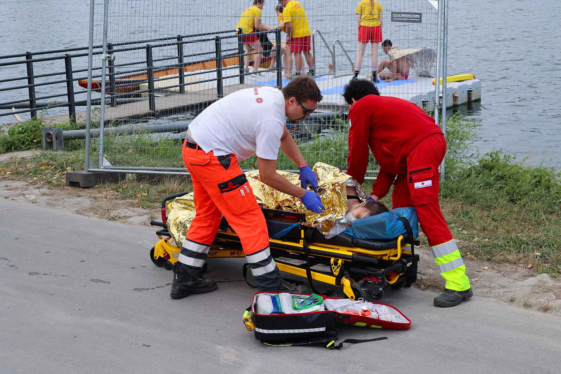 Einsatzvorführung Wasserrettung: Eine verunfallte Schwimmerin liegt mit Rettungsdecke auf der Trage und wird von zwei Sanitätern versorgt.