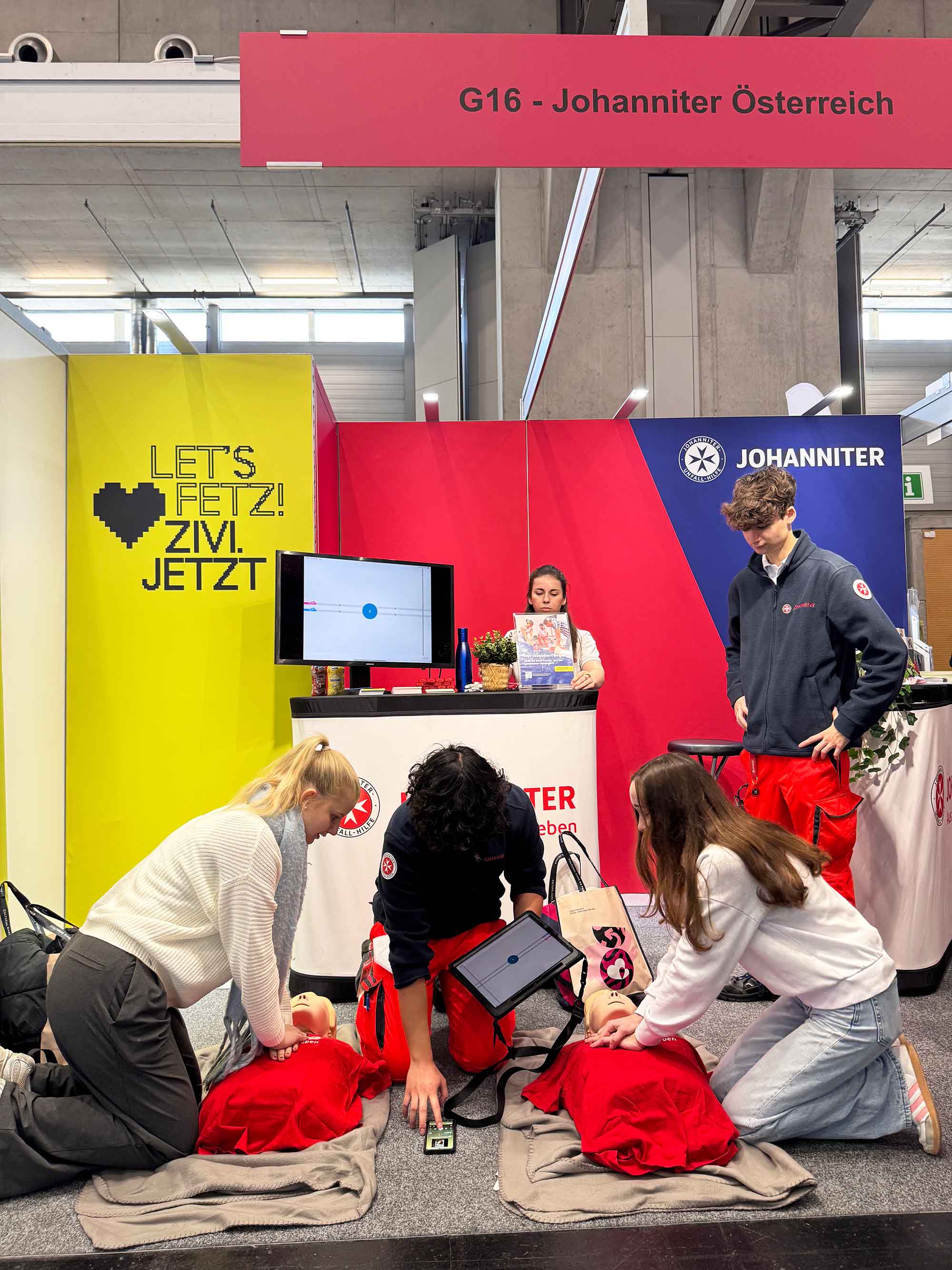 Zwei Messebesucherinnen machen das Reanimationsduell, angeleitet von einem Johanniter-Zivildiener.