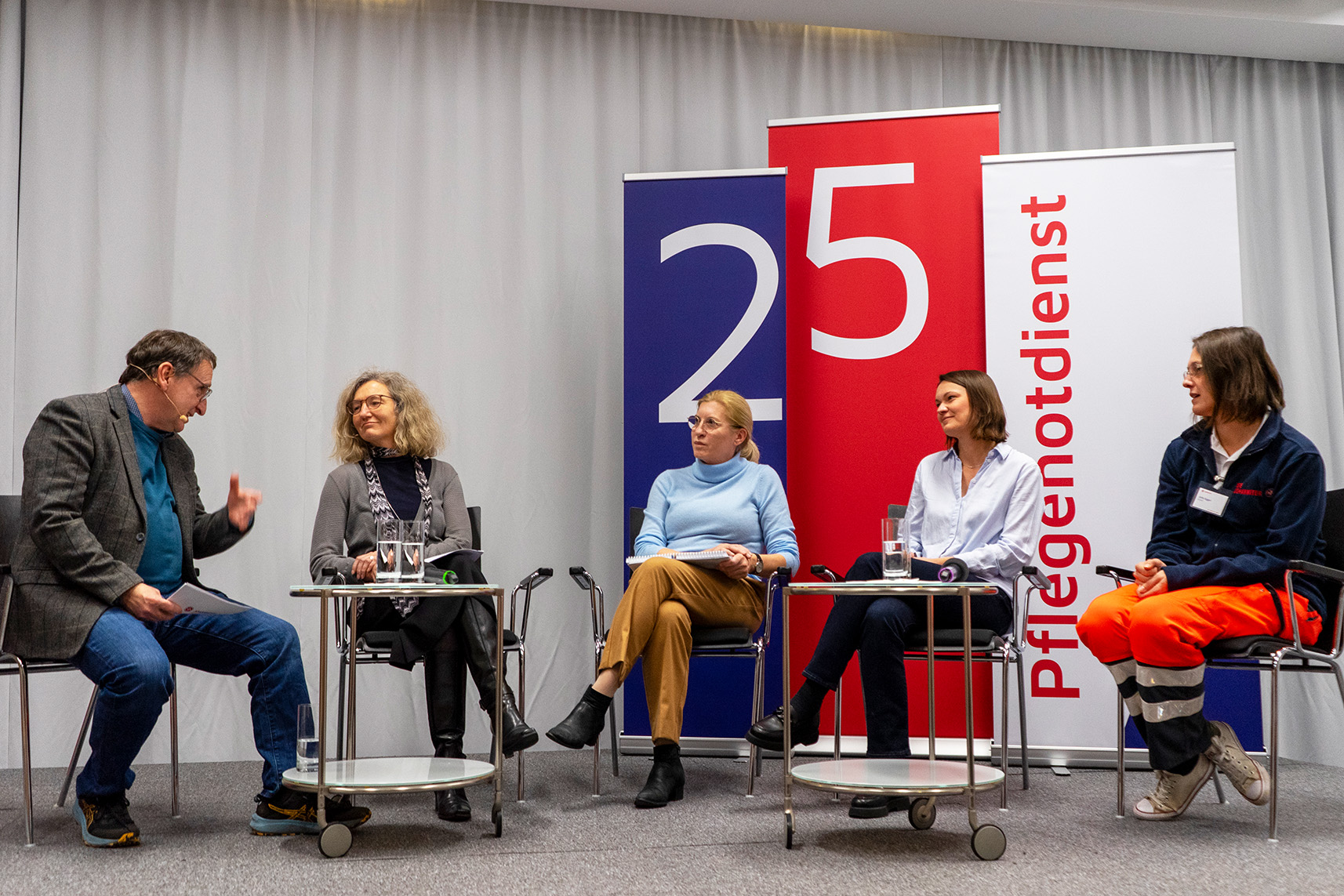 Der Moderator und die Panel-Gäste sitzen in einem Halbkreis auf der Bühne.