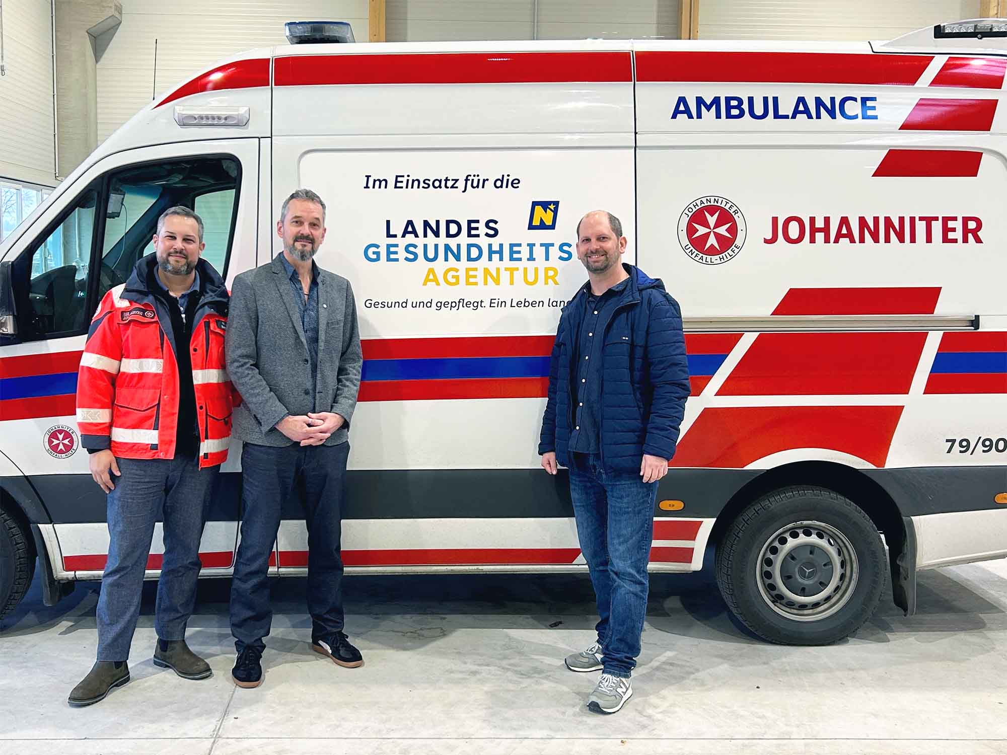 Der Bürgermeister von Spillern steht gemeinsam mit zwei Johannitern vor einem Johanniter-Rettungsauto.